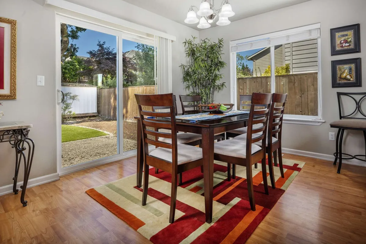 A look at the dining table set beneath a chandelier, with windows and decorative plants nearby. The space is styled for both everyday meals and celebratory gatherings, with a view of the garden outside.