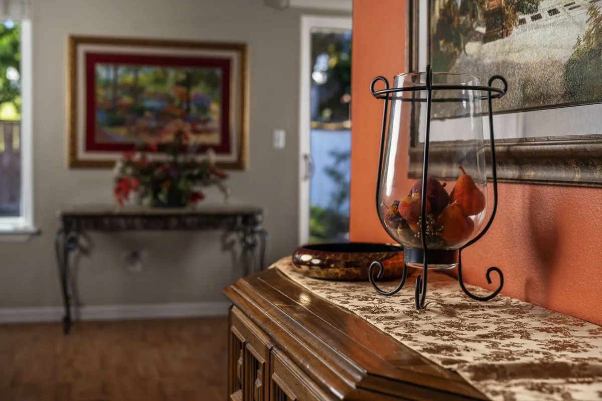 A warmly lit console table topped with a decorative vase filled with fruits, set against framed artwork. The inviting setting suggests a space for gathering with friends and sharing stories over drinks, echoing the convivial spirit of local tasting rooms and eateries.