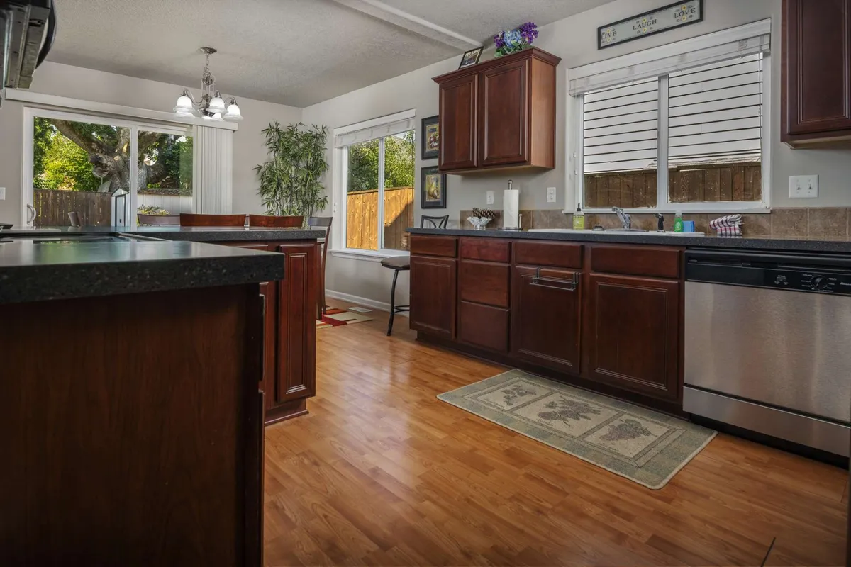 A perspective of the kitchen and dining area, showcasing wooden cabinets, a spacious kitchen island, and windows that invite in natural light. The setup is designed for cooking, family gatherings, and casual meals.