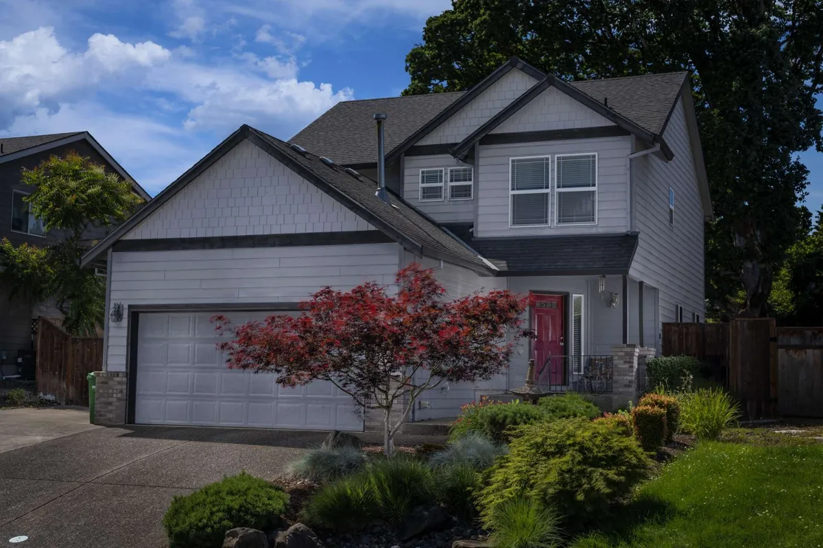 The image displays the welcoming exterior of a beautifully maintained two-level home, featuring a charming front door, lush landscaped gardens, and an attached garage. The inviting porch hints at a perfect spot to relax and enjoy Oregon sunsets, while the spacious front yard sets the scene for outdoor leisure and family gatherings.