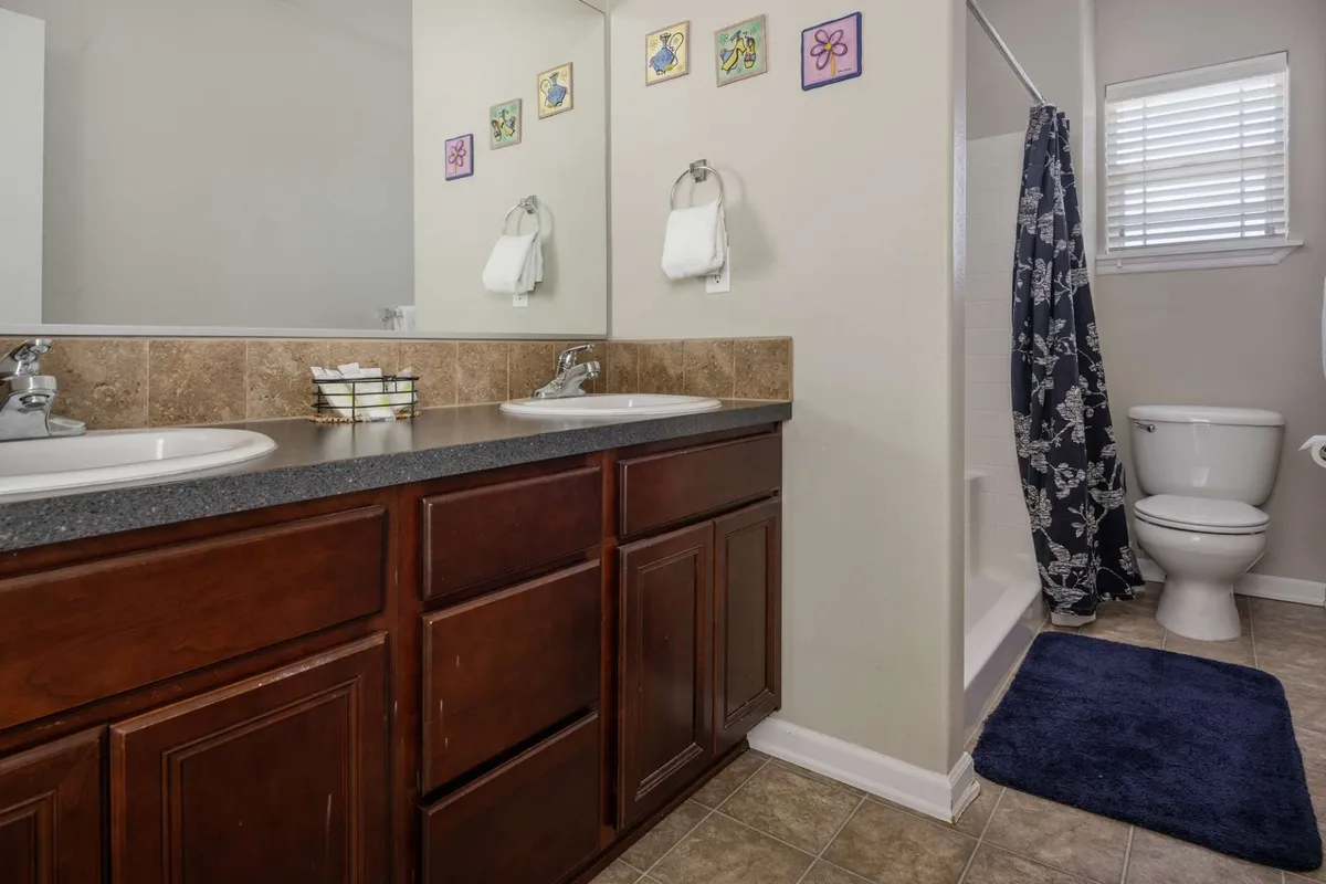 A well-appointed bathroom featuring a double sink vanity, decorative wall art, a shower curtain, and a toilet. The space is organized, fresh, and designed for relaxation as well as efficient morning routines.